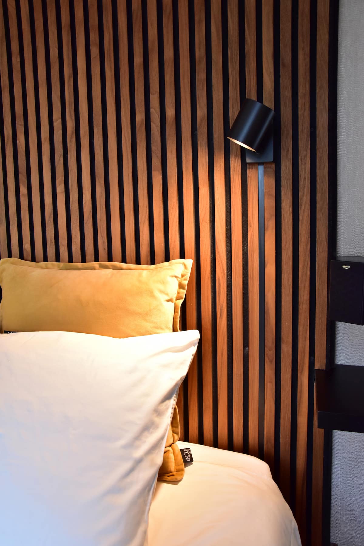Bed detail met leeslamp en houten wandpaneel